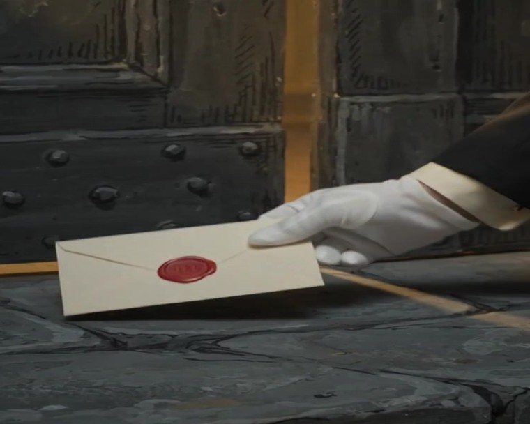 A white-gloved hand setting down a cream envelope sealed with red wax